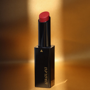 SUN KISS TINT DARK DAHLIA vitamin D infused lip tint standing upright against a background of gold silk standing upright in a beam of sunlight.