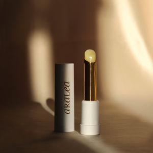 SUN KISS BALM vitamin D infused lip balm stands upright in a beam of sunlight against a background of deep gold silk fabric.
