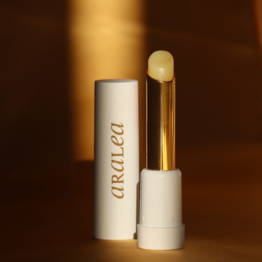 SUN KISS BALM vitamin D infused lip balm stands upright in a beam of sunlight against a background of deep gold silk fabric.