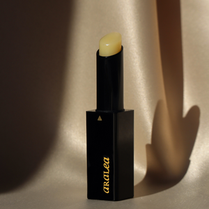 SUN KISS BALM vitamin D infused lip balm stands upright against pale yellow-gold fabric in direct sunlight.