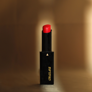 SUN KISS TINT CORAL vitamin D infused lip tint stands upright against pale gold silk fabric in a beam of sunlight.