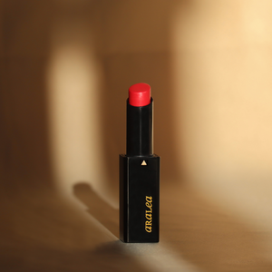 SUN KISS TINT CORAL vitamin D infused lip tint stands upright against pale gold silk fabric in a beam of sunlight.
