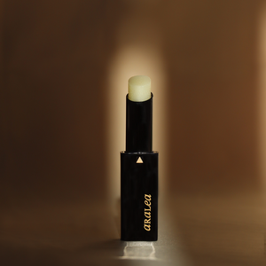 SUN KISS BALM vitamin D infused lip balm stands upright against pale yellow-gold fabric in a beam of sunlight.